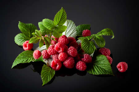 Fresh raspberries with leaves on a black reflective background.
