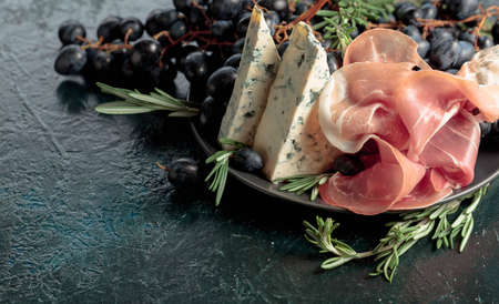 Prosciutto with blue cheese, grapes, and rosemary, on vintage background.の写真素材
