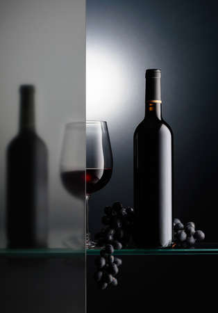 Bottles and a glass of red wine with a bunch of blue grapes. The still life is partially covered by a frosted glass. Copy space.の写真素材