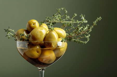Green olives in a glass bowl garnished with hyme. Copy space.の写真素材