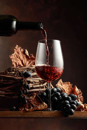 Wine is poured into a glass. Red wine and bunch of grapes on vintage wooden table.の写真素材