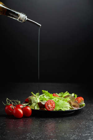 Green salad with tomatoes cherry is poured with vegetable oil. Vegetarian salad on a black background.の写真素材