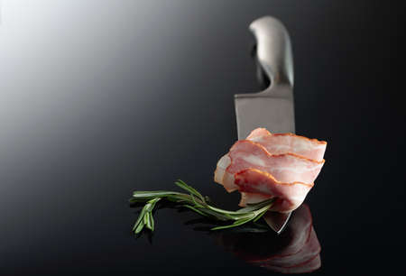 Bacon with rosemary on a kitchen knife. Reflective background.の写真素材