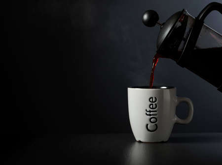 Pouring French press coffee into a cup on a black table. Copy space.の写真素材