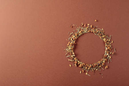 Herbal tea is scattered on a brown background. Round copy space. Top view.