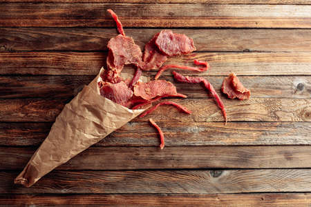 Slices of spicy dry-cured meat in a paper bag on an old wooden table. Top view.の写真素材
