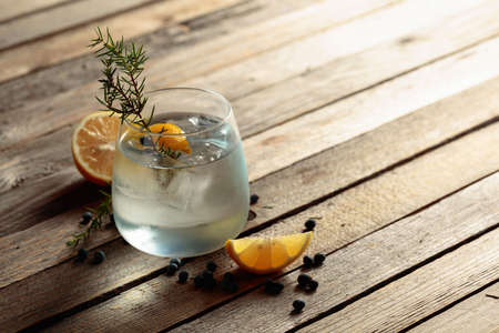 Gin tonic cocktail with lemon, juniper branch,  and ice on rustic wooden table, copy space. Iced...