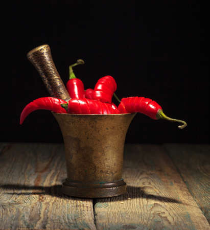 Red chili pepper in old copper mortar on a black background.の写真素材