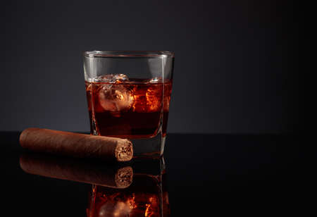 Whiskey with ice and cigar on a black reflective background.の写真素材