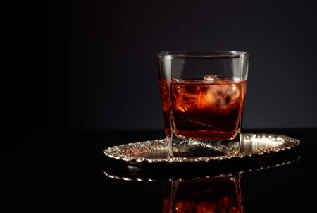 Whiskey with ice on a silver tray. Copy space.