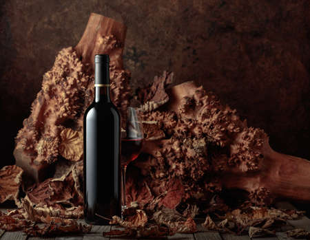 Bottle and glass of red wine on an old wooden table. In the background are old snags and dried-up...