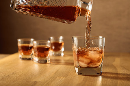Whiskey is poured into a dammed glass with natural ice. Glass of whiskey on an oak table.