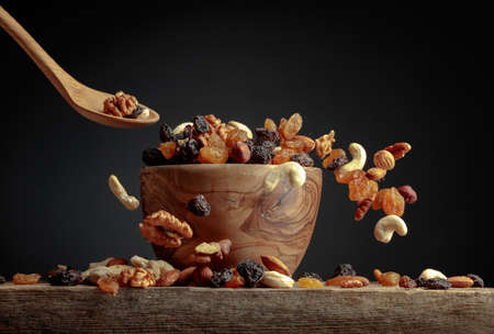 Flying dried fruits and nuts. The mix of dried nuts and raisins in a wooden bowl. Copy space.