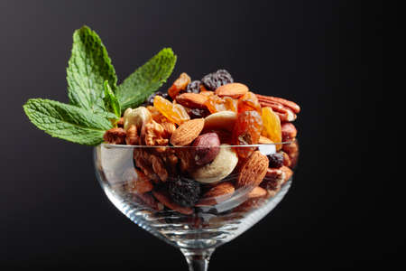The mix of nuts and raisins in a glass bowl is garnished with mint on a black background.の写真素材