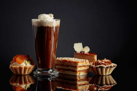 Coffee drink with whipped cream and cakes on a black reflective background. Copy space.