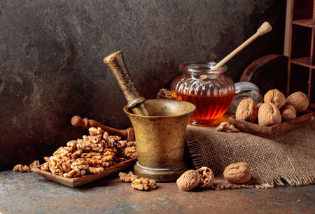 Walnuts, old brass mortar, and honey on a kitchen table.の写真素材