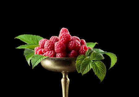 Fresh raspberries with leaves in an old brass dish on a black background.の写真素材