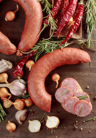On a old wooden table sausage with bread, rosemary, onion, garlic and pepper. Top view.