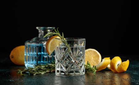 Gin tonic cocktail with lemon and rosemary on a black background. Copy space.