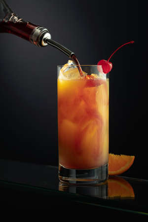 Tequila Sunrise alcoholic cocktail in a tall glass. Grenadine is poured into a glass.の写真素材