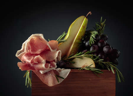 Prosciutto with rosemary, pear, and grapes on ablack background.の写真素材