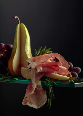 Prosciutto with rosemary, pear, and grapes on a glass table.の写真素材