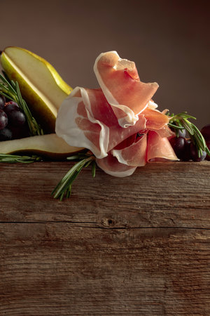 Prosciutto with rosemary, pear, and grapes on an old wooden table. Copy space.の写真素材