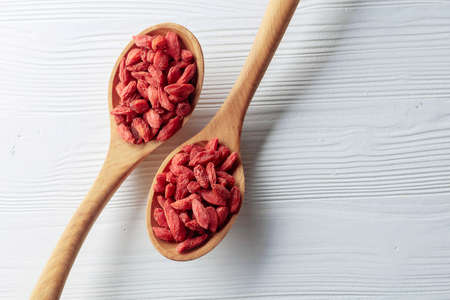 Dried goji berries in wooden spoons on a white wooden table. Top view.の写真素材