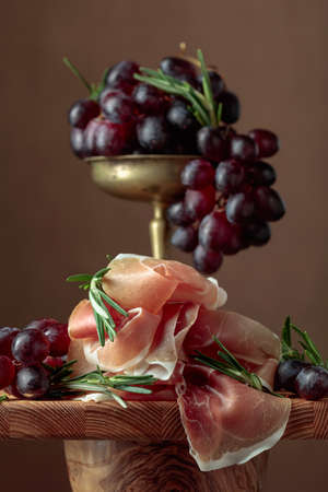 Prosciutto with grapes and rosemary on a wooden table.の写真素材