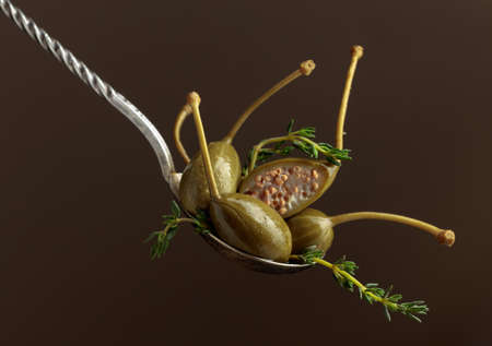 Large pickled capers with thyme in spoon on a brown background. Copy space.
