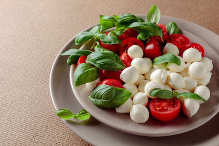 Caprese salad with tomato, mini mozzarella and basil on a brown background. Italian food and healthy...