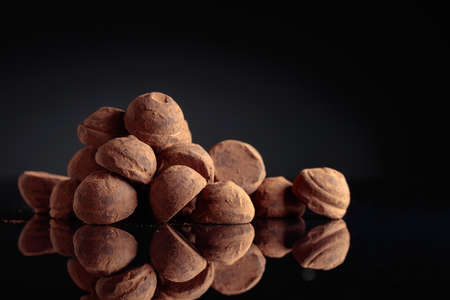 Tasty chocolate truffles powdered with cocoa on a black reflective background.の写真素材