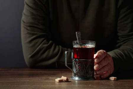 Man holds a traditional Russian glass holder with hot tea. Concept of the theme of despair and thinking. Copy space.の写真素材