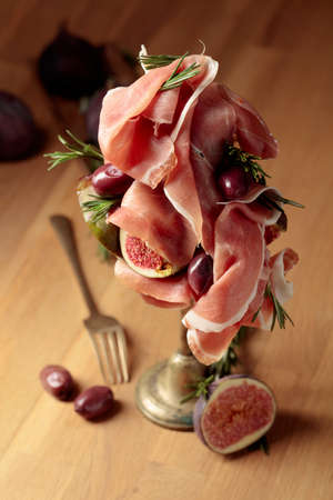 Prosciutto with figs, rosemary, and red olives on a old wooden table. Mediterranean snacks.の写真素材