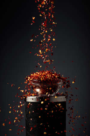 Flakes of red hot chili pepper are poured into a small glass bowl.の写真素材