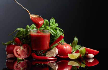Spicy tomato sauce with ingredients. Fresh tomatoes, red pepper, garlic, basil, and lime on a black...