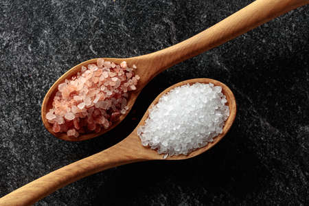 Pink and sea salt in wooden spoons on a black stone background.の写真素材