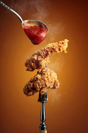 Delicious crispy fried chicken with tomato sauce. Fried chicken with ketchup on a fork.の写真素材