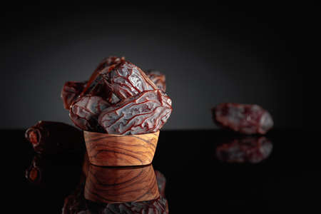 Raw ripe dates fruits on a wooden dish on a black background. Copy space.