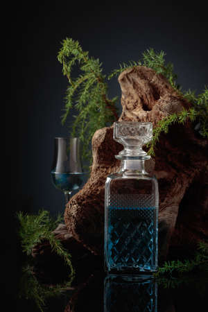 Blue gin on a black background. Juniper branches and old driftwood are in the background. Focus on the foreground.の写真素材
