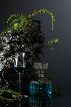 Blue gin on a black reflective background. Juniper branches and grey stone are in the background.の写真素材