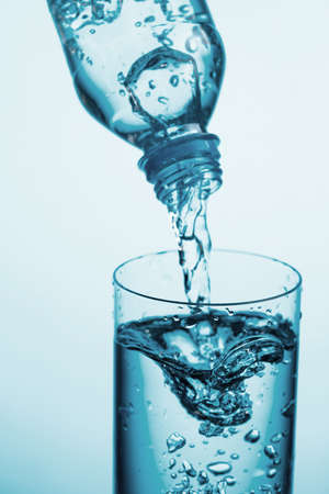 Pouring water from a bottle into glass on a blue background. Copy space.の写真素材