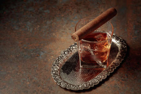 Whiskey with ice and cigar on a rusty metal table.