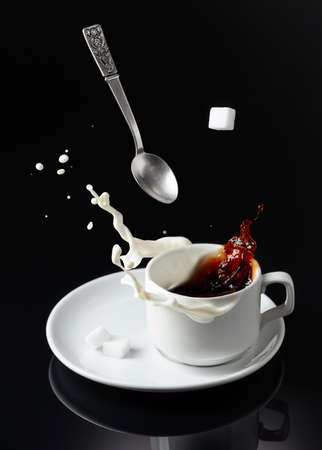 Cup of coffee on a black reflective background. Coffee with milk splashing.の写真素材