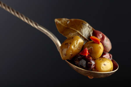 Spicy olives in a big spoon on a black background.の写真素材