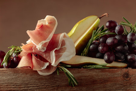 Prosciutto with rosemary, pear, and grapes on an old wooden table. Copy space.の写真素材