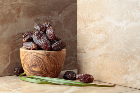 Fresh dates fruit in a wooden dish on a beige ceramic table. Copy space.