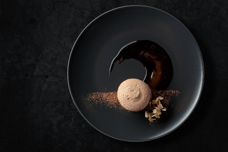 Macaroon on a black plate garnished with chocolate sauce and cocoa powder. Black stone background with copy space.の写真素材