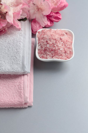 Spa composition with pink Himalayan salt, flowers, and towel. Copy space.