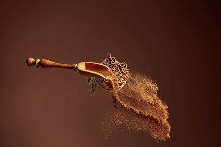 Cinnamon powder is poured out of the wooden spoon. The ground cinnamon and cinnamon sticks, tied with jute rope on a brown background.の写真素材
